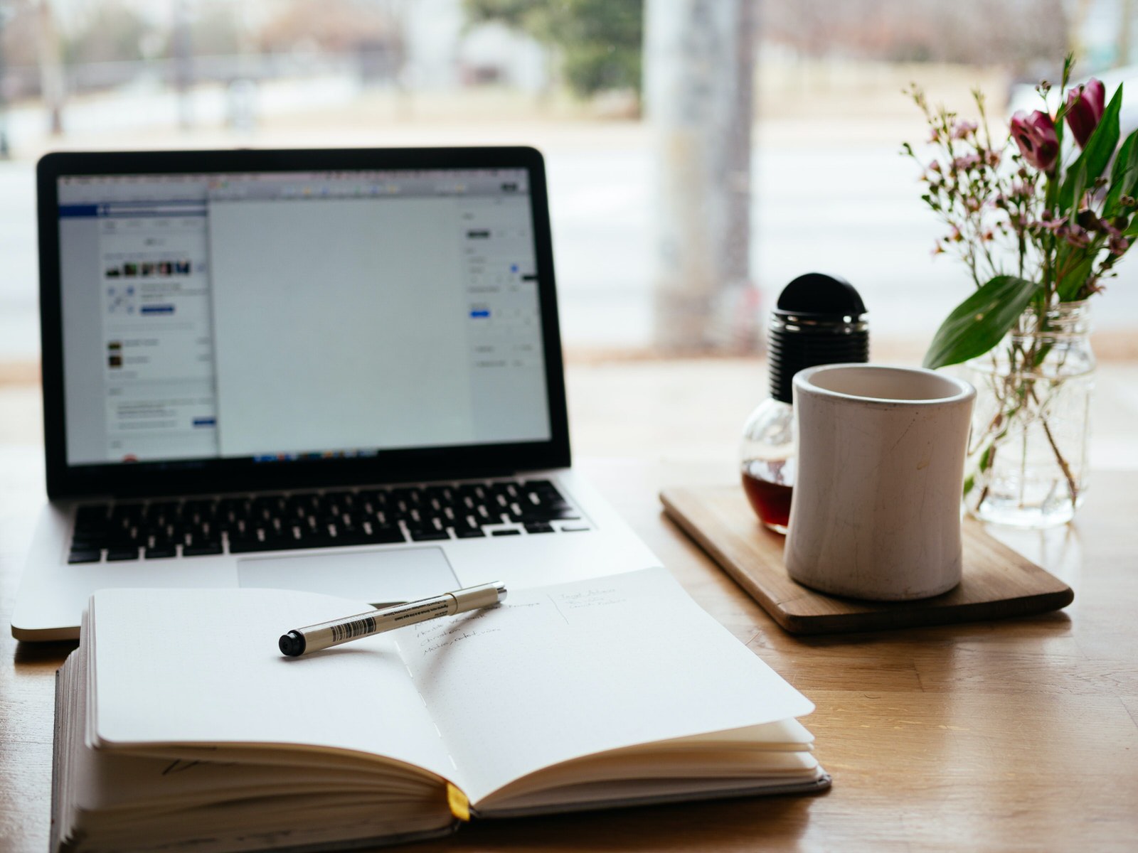 Laptop mit Notizbuch, Tasse und Blume